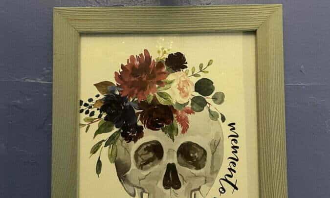 Framed art of skull with flowers and "memento mori" hanging on wall